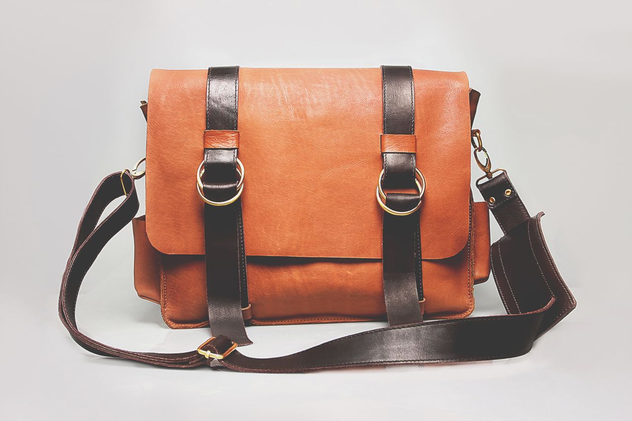 Services Elegant brown leather briefcase with dark straps and metal buckles, ideal for fashion and business.